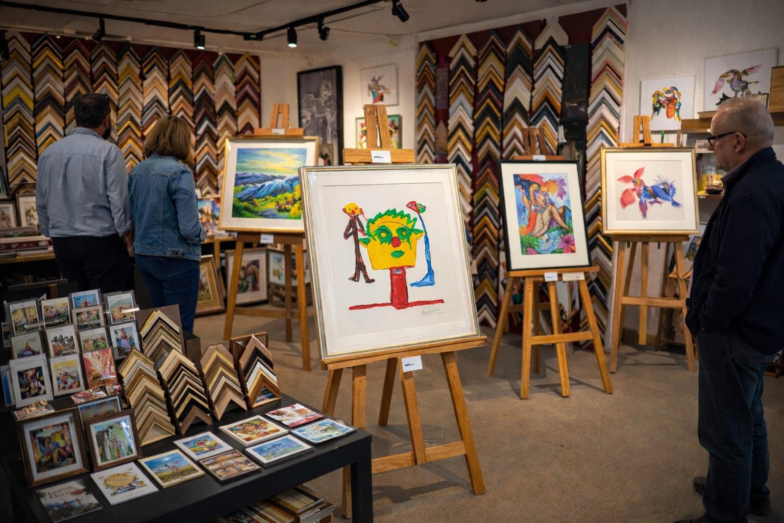 Galeria La Pătrat — lucrări înrămate expuse pe șevalete, pereți plini de profile de rame.